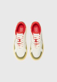 Hvite perforerte sneakers med røde detaljer, polstret krage, beige mellomsåle og gul gummisåle. Merkevarelogo på tungen.