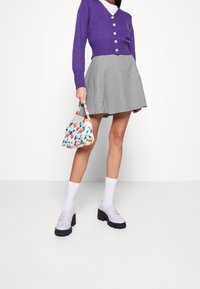 Lila gestrickte Strickjacke mit Knopfdetails, kariertem Rock, gemusterter Handtasche mit Tulpen und lavendelfarbenen Slippern mit dicken Sohlen.