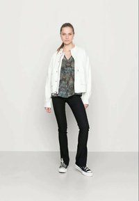 Casaco bomber branco sobre uma blusa azul com padrão, combinado com jeans pretos largos e ténis preto e branco. Design minimalista, estilo casual.