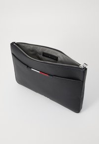 Pochette en cuir noir avec une finition texturée, dotée d'une fermeture éclair argentée et d'une petite poche avant avec des accents bleu, blanc et rouge.