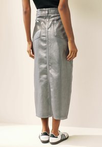 Metallic silberner Midi-Rock mit hoher Taille, zwei Gesäßtaschen, glatter Textur und einer Mittelnaht, die hinten entlang läuft.