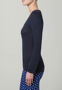 Marineblaues Langarmoberteil aus einem weichen, leichten Stoff mit einem V-Ausschnitt und Knopfakzenten, kombiniert mit einer Hose im gepunkteten Muster.