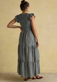 Schwarz-weißer Gingham-Maxikleid mit Flatterärmeln und gestuftem Rock, ausgestattet mit einem gerafften Oberteil und Rüsche am Saum. Getragen mit braunen Schuhen.