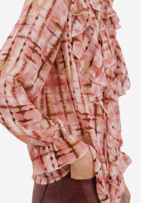 Růžová halenka s volánkovými doplňky a batikovaným vzorem v odstínech hnědé. Vyrobená z lehké, texturované látky.
