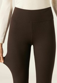 Bruine geribbelde legging met een hoge tailleband, gemaakt van rekbare stof. De textuur is glad en sluit nauw aan rond de benen.