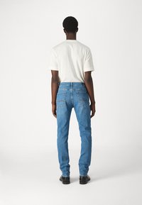 Wyblakłe niebieskie dżinsy o prostym kroju nogawki, z tylnymi kieszeniami ozdobionymi falistym szwem, w zestawie z gładką białą koszulą.