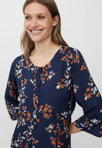 Marinblå klänning med orange, vit och blå blommönster, med rund halsringning och knappslå, tillverkad i ett lätt tyg.