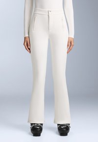 Fehér, testhezálló nadrág magas derékkal, két elülső cipzáras zsebbel és harang alakú lábakkal. Simogatós, rugalmas anyagból készült.