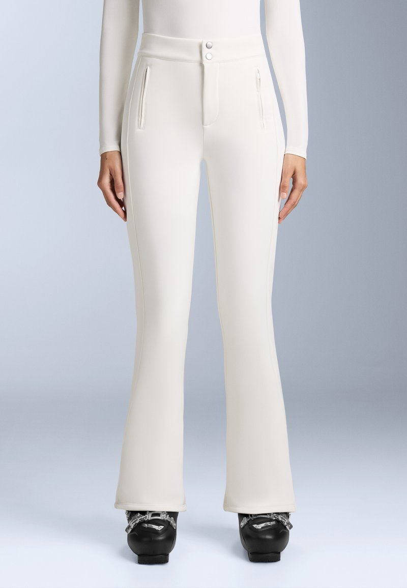 Fehér, testhezálló nadrág magas derékkal, két elülső cipzáras zsebbel és harang alakú lábakkal. Simogatós, rugalmas anyagból készült.