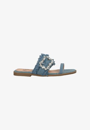 Denim slide sandal featuring frayed edges, a wide band with a large rhinestone buckle, flat sole, and light blue color.