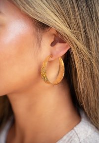 Orecchini a cerchio in oro con superficie texture, grande forma a mezzaluna e finitura lucida, appesi a un orecchio forato.