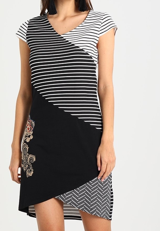 Femme portant une robe à manches courtes rayée noir et blanc avec broderie florale et un ourlet asymétrique à motif géométrique.