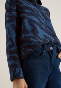 Camicia a bottoni blu e navy con un motivo, dal taglio rilassato, abbinata a jeans blu scuro con tasca frontale e dettagli con bottone.