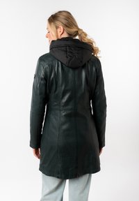 Abrigo de cuero en verde oscuro con una capucha acolchada negra. Presenta detalles de costura y un diseño ajustado. Textura suave con un acabado ligeramente brillante.