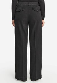 Szerokie czarne spodnie wykonane z gładkiego materiału, z dwoma tylnymi kieszeniami zapinanymi na guziki oraz przeszywaną talią.