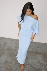 Lys blå ribbestrikka kjole med off-shoulder design og volangerm med sølvprikk accenter. Myk tekstur, gulvlengde.