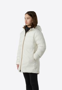 Valge kapuutsiga polsterdatud jope, millel on tõmbluku sulgur ja küljetaskud, kombineeritud musta topi ja mustade retuusidega.