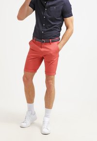 Mörkblå knapp-up skjorta för män, korallfärgade shorts och vita sneakers. Shortsen har en slim fit. Texturen är slät, med uppvikta fållar och ett vävt bälte.