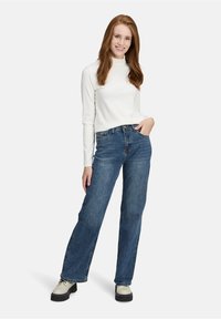 T-shirt blanc à manches longues côtelé et jeans bleu à jambes larges, associés à des chaussures beiges à lacets. Couleurs neutres et coupe décontractée.