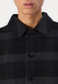Black and gray plaid wool coat with a structured collar. Features four black buttons down the front and a soft texture.