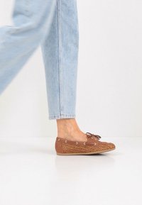 Chaussures plates marron à lacets avec détails tissés, tige en cuir lisse et semelle en caoutchouc, présentées aux côtés d'un jean bleu clair.