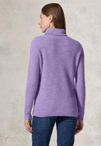 Pull en laine violet avec un col montant, motif texturé, poignets et ourlet côtelés, associé à un jean bleu foncé.