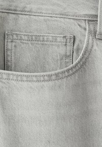 Gros plan sur un tissu en denim gris clair montrant une petite poche intérieure cousue à l'intérieur d'une plus grande poche avant avec des détails de couture visibles.