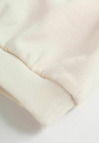 Ärmels eines sweatshirts aus baumwolle in cremefarbe mit geripptem bündchen vor weißem hintergrund