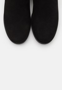Un par de botas negras de ante con puntas redondeadas, mostradas desde arriba sobre un fondo blanco.