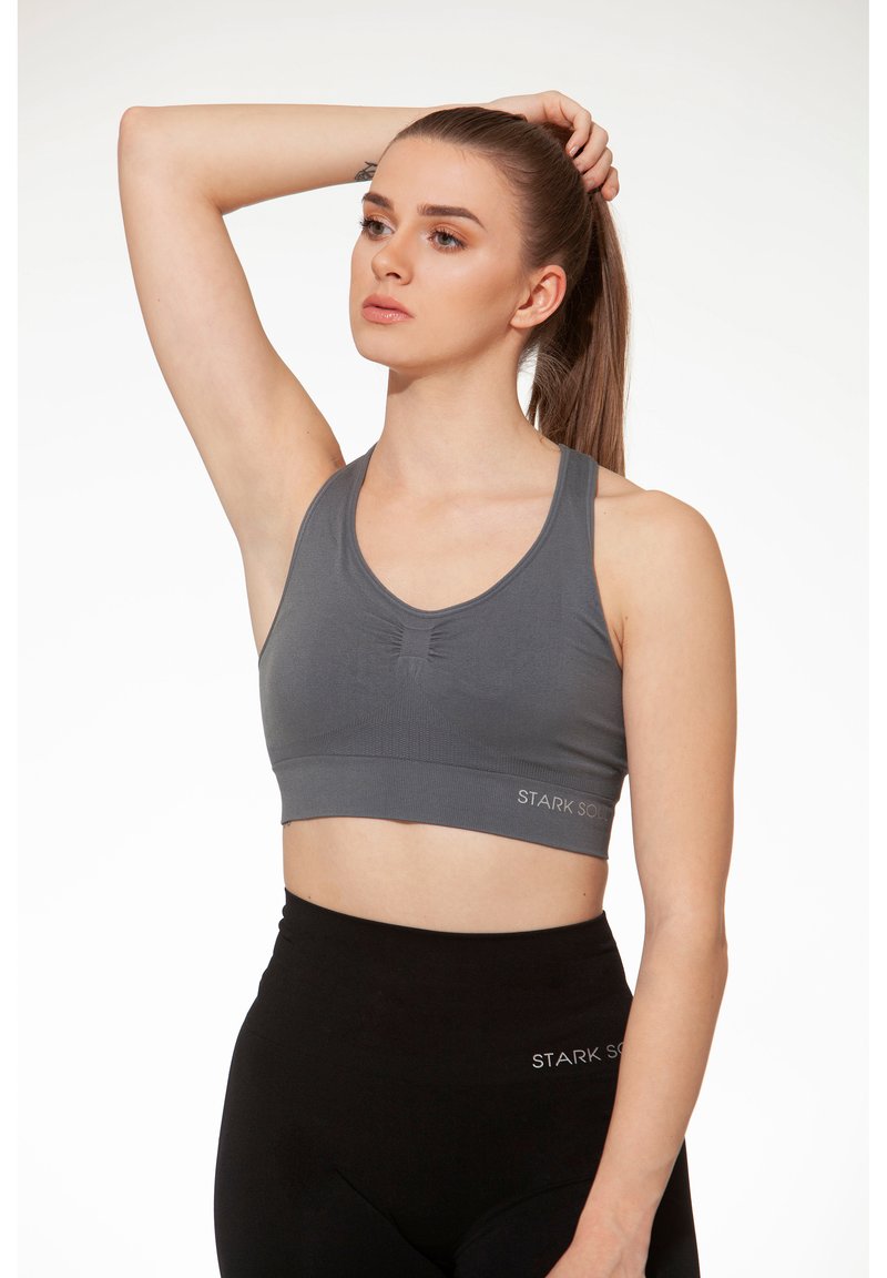 Sostenitore sportivo grigio con design a V, tessuto textured e dettaglio logo all'orlo, abbinato a leggings neri a vita alta.