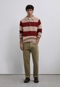 Jersey de punto con rayas rojas y beige, diseño con cuello y tres botones. Combinado con pantalones beige y zapatos marrones. Corte moderno.