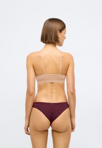 Biustonosz w jasnobeżowym materiale z cienkimi ramiączkami, w połączeniu z bordowymi slipami bikini. Gładka tekstura i prosty, minimalistyczny design.