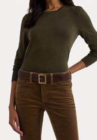 Bruna kordflädesbyxor i kombination med en olivgrön ribbad långärmad topp och ett mörkbrunt bälte med en texturerad guldlåsning.