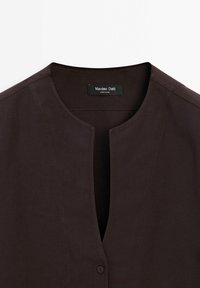 Chemise marron foncé à col en V avec une fermeture à un seul bouton et une étiquette Massimo Dutti à l'intérieur du col.