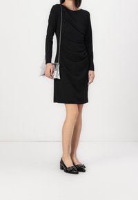 Černé šaty s dlouhým rukávem a z řaseným materiálem. Vydané s lesklými černými botami na blokovém podpatku a kovovou stříbrnou kabelkou s řetízkovým popruhem.