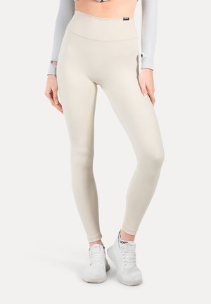 Højtaljede, beige leggings lavet af strækbart stof, med en glat tekstur og et elegant design. Båret med hvide sneakers.