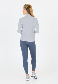 Lys grå jakke med vandret polstring, parret med mørkeblå leggings. Reflekterende løbesko med sølvaccenter fuldender outfittet.
