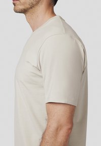 Beżowa koszulka z krótkim rękawem o okrągłym dekolcie, wykonana z miękkiego materiału, z płaskimi szwami i dopasowanym krojem.