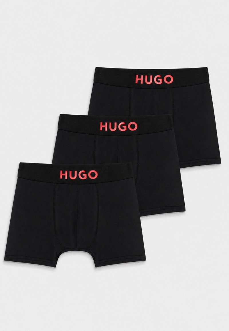 Trois boxers noirs avec le logo rouge HUGO sur la ceinture, disposés en chevauchement sur un fond blanc.