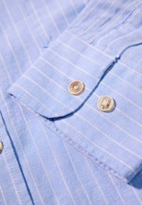 Lichtblauwe gestreepte blouse met knoop-om-nu collar, twee crèmekleurige knopen, zachte stoftextuur en gelijkmatig verdeelde witte strepen.