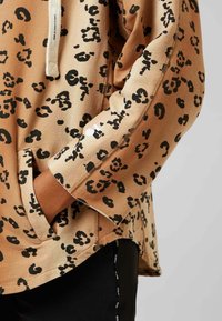 Bluza w panterkę w kolorze brązowym z czarnymi plamami, z przednią kieszenią i kapturem ze sznurkiem, luźny krój, rękawy z mankietami.