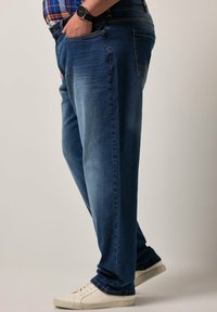 Modré džínové kalhoty s volným střihem, předními kapsami a vybledlou texturou. Kombinované s bílými teniskami, zobrazené ze strany.