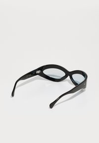 Lunettes de soleil noires avec une forme ovale allongée, monture en plastique brillante et verres teintés bleus. Des accents métalliques sur les côtés présentent des détails de marque.