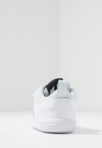 Białe sportowe buty z teksturowaną skórzaną cholewką, siateczkowymi akcentami, czarną pętelką na pięcie oraz amortyzowaną podeszwą z detalem logo.
