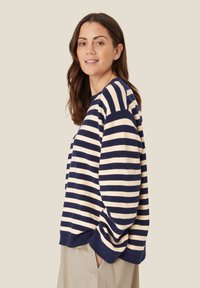 Gestreifter Pullover in Marineblau und Creme, gestrickte Textur, lockere Passform, überschnittene Schultern, gerippte Bündchen, sichtbare Nahtdetails, kombiniert mit hellen Hosen.