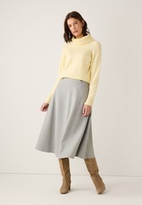 Yellow turtleneck sweater made of soft, textured fabric, paired with a gray A-line skirt and tan knee-high heeled boots.
