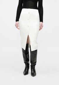 Fehér bordázott midi szoknya elülső hasítékkal és öt gombbal. Magas, fekete, testhez simuló bőr csizmával párosítva, meghosszabbított formában, sima textúrával.