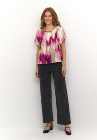 Short-sleeve top in cream, pink, and grey abstract pattern; paired with high-waisted black wide-leg jeans and black block-heeled shoes.