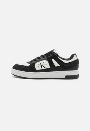 Sneaker bianca e nera con materiali in camoscio e pelle, punta perforata, lacci piatti e dettagli del logo sul lato e sulla linguetta.