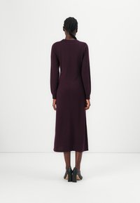 Robe ajustée à manches longues en jersey prune profond, avec une coupe droite et une longueur mi-mollet, associée à des chaussures à talons carrés noires.